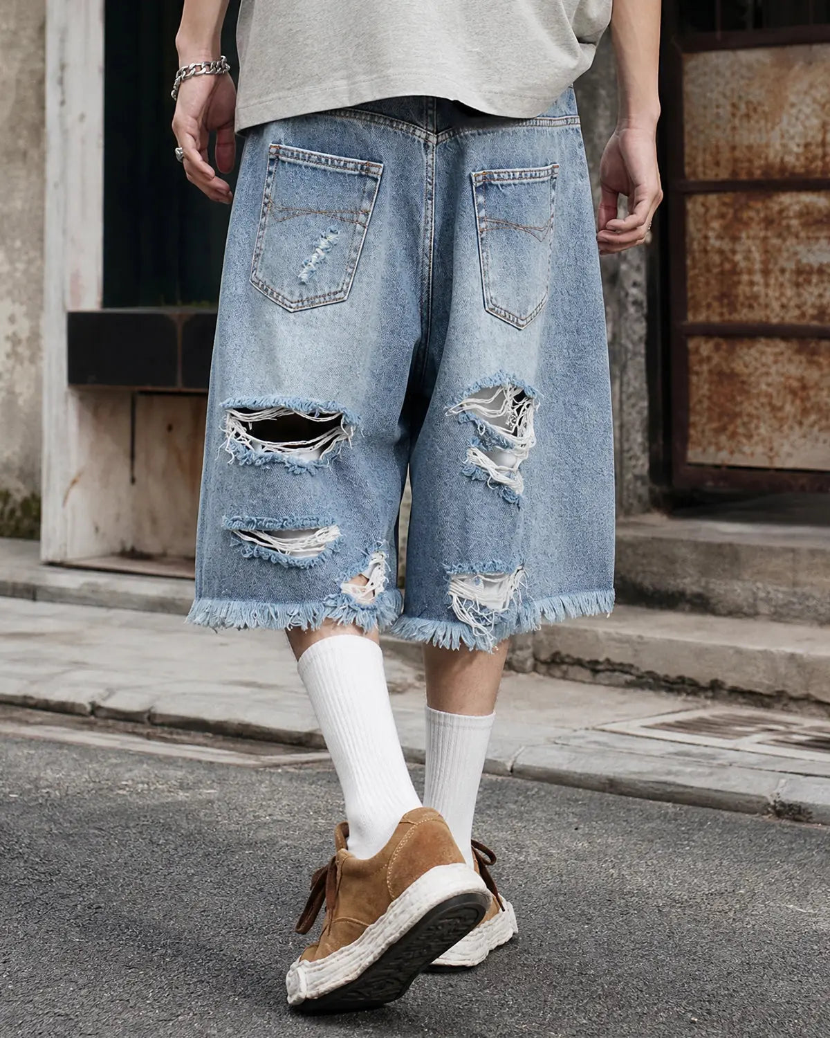 Distressed baggy jorts by INFLATION with adjustable waist tabs, laid flat to showcase frayed denim and relaxed fit.