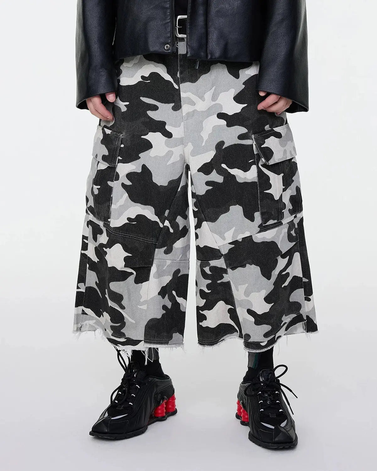 Glitter camo cargo longline shorts by INFLATION, featuring shiny fabric, multiple pockets, and a relaxed streetwear style.